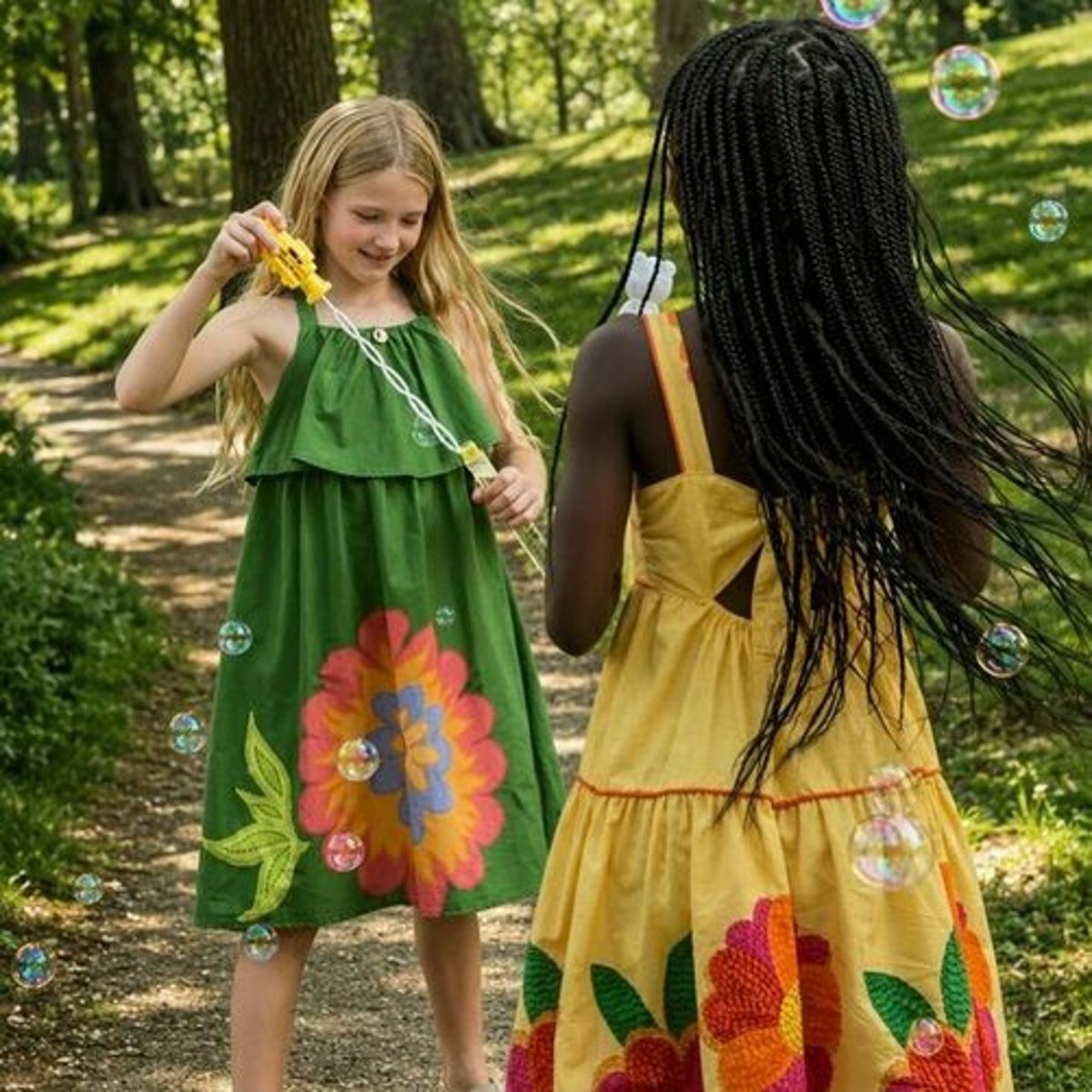 Duas meninas brincam ao ar livre com vestidos estampados de flores da marca Camu Camu